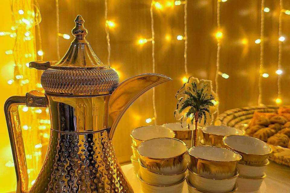 دلة قهوة ذهبية وفناجين على صينية وسط أضواء احتفالية دافئة