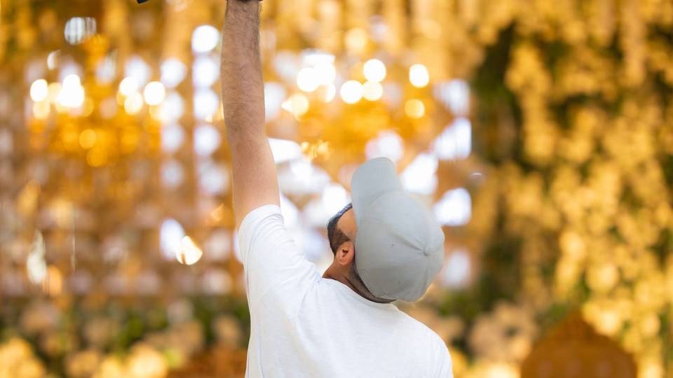 مصور يرفع كاميرته لتصوير قاعة مزينة بإضاءة ذهبية دافئة