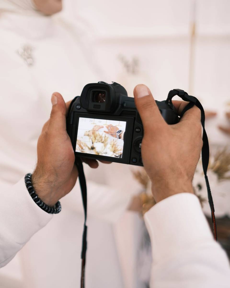 رجل بالثوب والشماغ يحمل كاميرا احترافية ويراجع الصورة على شاشتها