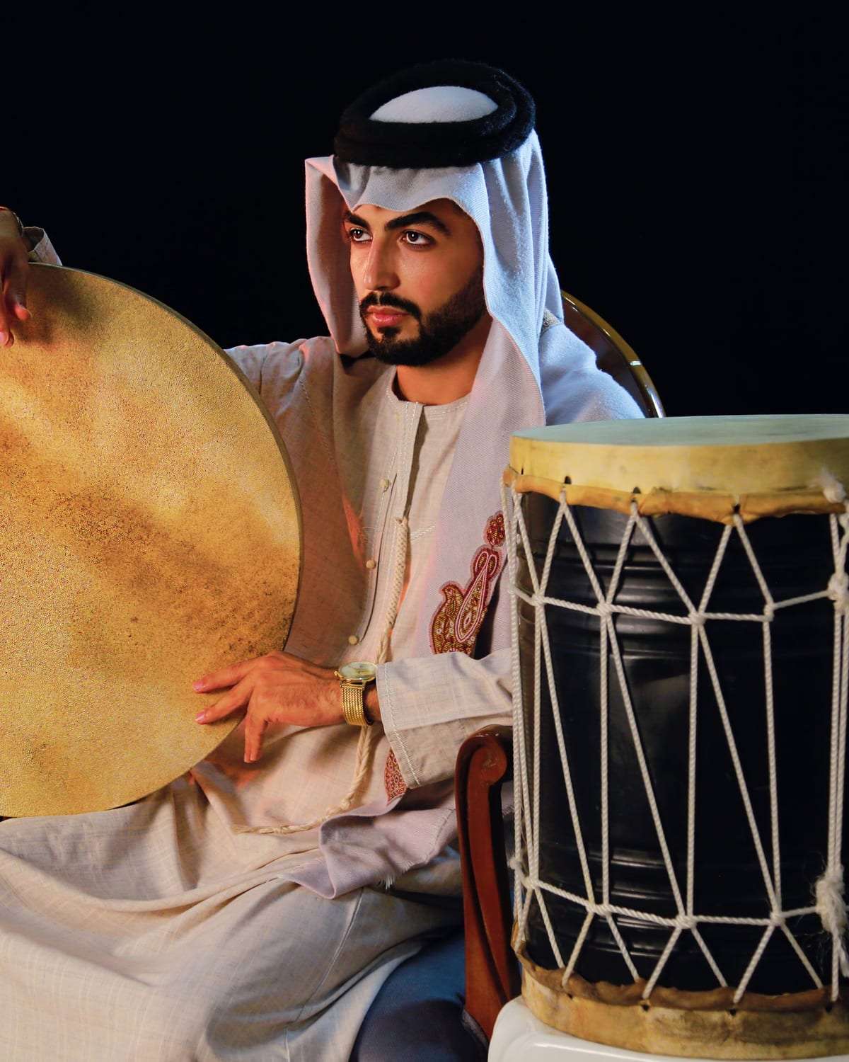 رجل بالزي الخليجي يحمل دفاً وبجانبه طبل تقليدي