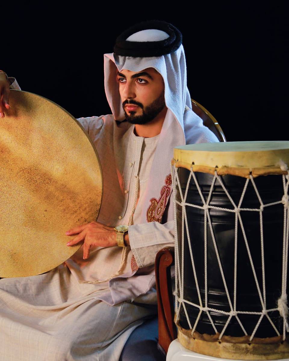 رجل بالزي الخليجي يحمل دفاً وبجانبه طبل تقليدي